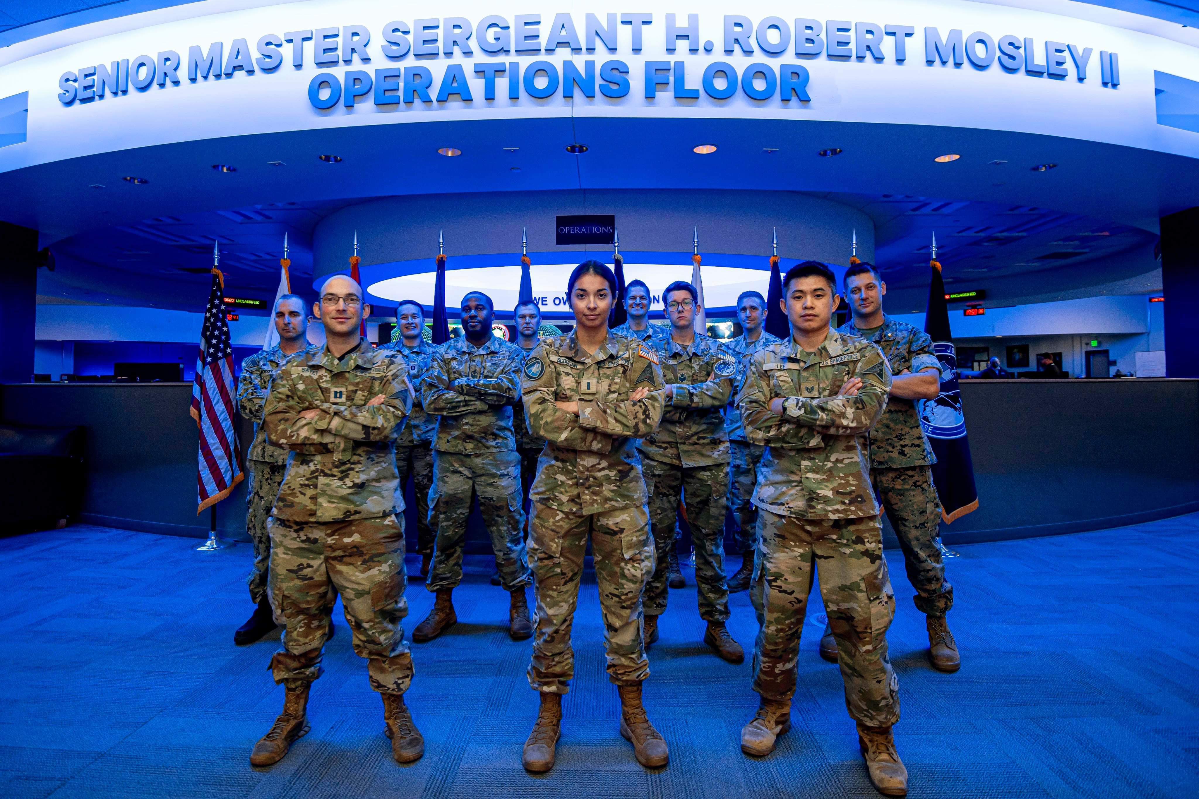 U.S. Space Force Tech. Sgt. Peter Lee, front right, Space Delta 2, Detachment 1, flight chief of operations, poses for a photo with team members in front of the National Space Defense Center operations floor at Schriever Space Force Base, Colorado, Oct. 5, 2022